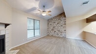 This well-designed 2-bedroom, 1-bathroom home in Round Rock, Texas offers a thoughtful single-level layout that maximizes every inch of its comfortable footprint. The living room immediately impresses with vaulted ceilings, a ceiling fan with light fixture, and a tile-surround fireplace with a classic wood mantel — creating a warm, inviting atmosphere. The space flows naturally toward the entry, which features wood-look flooring that contrasts nicely with the plush carpeting found throughout the rest of the home.

A standout feature of the primary bedroom is its dramatic vaulted ceiling, a bold exposed brick accent wall, and a ceiling fan, all complemented by a large window that invites natural light. The second bedroom is equally comfortable, offering carpet flooring, a ceiling fan, and its own generously sized window with blinds. Both rooms provide a calm, neutral palette well-suited for a variety of furnishing styles.

The kitchen is efficiently arranged with dark wood cabinetry, light countertops, wood-look flooring, and white appliances including a refrigerator and electric range. The full bathroom features a tub/shower combo with clean white tile surrounds. Hallways connect the rooms smoothly, rounding out this functional and characterful home.