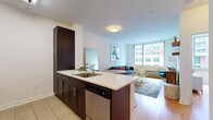 This well-appointed single-floor residence offers a thoughtfully designed open-concept layout that seamlessly connects the kitchen, dining, and living areas. The kitchen is outfitted with dark espresso cabinetry, stainless steel appliances including a refrigerator, microwave, and range, and a peninsula with a light-toned countertop that doubles as a breakfast bar with seating. Hardwood flooring flows throughout the main living areas, adding warmth and continuity to the space.

The living room is bright and inviting, anchored by a large picture window that frames urban city views and allows natural light to fill the room. The two bedrooms are generously proportioned, each featuring oversized windows with city-facing views, hardwood floors, and a clean, neutral palette that creates a calm and restful atmosphere.

The bathroom is finished with tile flooring, a dark vanity with a light countertop, a full mirror, and a shower-tub combination, maintaining the consistent modern aesthetic found throughout the residence.

The entryway provides a practical transition into the home, with access to an electrical panel and direct sightlines into the open kitchen and living area. Overall, the space presents a clean, contemporary design with a functional layout well-suited for comfortable urban living.