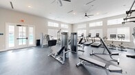 Located at 2213 Highland Forest Dr in Richmond, VA, this dedicated fitness center offers a generously sized, single-floor workout space designed to accommodate a full range of exercise needs. The facility is bathed in natural light streaming through a series of large, elevated windows fitted with blinds, creating a bright and energizing atmosphere throughout.

The space is thoughtfully organized into distinct workout zones. A strength training area features a multi-function cable machine, a power rack with weight storage, a full dumbbell rack, and adjustable benches — providing everything needed for a comprehensive resistance training session. Large wall-mounted mirrors enhance the sense of space and allow users to monitor their form.

The cardio section is equally well-appointed, housing multiple treadmills, an elliptical, and a stair climber, all from the Matrix brand. Ceiling fans positioned overhead ensure consistent airflow and comfort during intense workouts.

The flooring throughout is durable dark rubber, ideal for both heavy equipment and high-impact activities. Recessed lighting supplements the abundant natural light, while a direct exterior door provides convenient access. The clean, neutral color palette and modern finishes give the space a professional, welcoming ambiance suited for everyday fitness use.