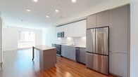 This contemporary 670 square foot apartment in Dublin, CA offers a thoughtfully designed living space. The open-concept layout seamlessly blends the living room and kitchen, creating an airy atmosphere enhanced by large windows that flood the space with natural light. Warm wood flooring extends throughout, adding a touch of elegance.

The kitchen boasts sleek, modern cabinetry in white and gray tones, complemented by stainless steel appliances including a refrigerator, built-in microwave, and dishwasher. Undercabinet lighting and a subway tile backsplash add to the refined aesthetic.

The apartment features two bathrooms, likely including an en-suite. While not explicitly shown, the bathrooms likely maintain the modern design theme of the rest of the space. A convenient in-unit laundry area with a stacked washer and dryer set is a notable amenity.

Storage solutions are integrated throughout, with sliding barn-style doors concealing closet spaces. The apartment's neutral color palette and clean lines create a canvas for personalization. Large windows in the living areas and bedroom offer views of the surrounding area and neighboring buildings.

This efficient floor plan maximizes the use of space, making it ideal for modern urban living. The property's location at Dublin Station suggests easy access to public transportation, adding to its appeal for commuters or those seeking a connected city lifestyle.