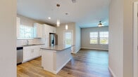 This single-floor residence is designed with a clean, contemporary aesthetic throughout. The open-concept layout connects the kitchen and living area seamlessly, creating a bright and functional space ideal for everyday living. The kitchen is well-appointed with white shaker-style cabinetry, dark countertops, a subway tile backsplash, and a full suite of stainless steel appliances, including a French door refrigerator, electric range, over-the-range microwave, and dishwasher. A center island with matching countertop provides additional workspace and casual seating. Warm hardwood-style flooring runs throughout the main living areas, adding continuity and visual warmth.

The living area benefits from natural light through multiple windows with horizontal blinds, and a ceiling fan overhead aids air circulation. An exterior door provides access to an outdoor area with views of the surrounding landscape. The bedrooms are generously sized, each equipped with ceiling fans and windows framing pleasant outdoor views; one bedroom features plush carpeting while another showcases hardwood-style flooring. The bathroom includes a full soaking tub and shower combination with clean white tile surround and chrome fixtures. Neutral wall tones throughout create a cohesive, move-in-ready atmosphere.