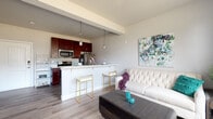This single-floor residence offers a thoughtfully designed open-concept layout that seamlessly connects the living, dining, and kitchen areas. The kitchen is a standout feature, showcasing rich dark cherry wood cabinetry, white countertops, and a full suite of stainless steel appliances including a refrigerator, electric range, and over-the-range microwave. A peninsula with bar seating and elegant pendant lighting serves as both a functional workspace and a casual dining spot, bridging the kitchen and living area with ease. The living space is warm and inviting, with light wood-style flooring that runs throughout the common areas, neutral gray walls, and ample room for comfortable furnishings. The bedroom is a serene retreat, featuring plush carpeting and a large window that allows generous natural light and views of the surrounding neighborhood. A closet provides convenient storage. The bathroom is finished with dark wood vanity cabinetry, a white countertop sink, and a full tub-shower combination with a curtain rod, complemented by dark hardwood-style flooring. Neutral tones and clean lines throughout the space create a cohesive, modern aesthetic that is both functional and welcoming.