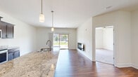 This single-floor residence offers a thoughtfully designed layout encompassing one bedroom, three bathrooms, two closets, and an in-unit laundry area. Rich hardwood flooring flows throughout the open-concept main living area, connecting the kitchen and dining space seamlessly. The kitchen is well-equipped with dark espresso cabinetry, granite countertops, stainless steel appliances including a refrigerator, electric range, microwave, and dishwasher, and pendant lighting overhead. A large sliding glass door in the living area floods the space with natural light and provides direct outdoor access and views of lush greenery. A built-in fireplace serves as a focal point in the living room, adding warmth and character. The spacious primary bedroom features plush carpeting, a ceiling fan, and a window with outdoor views, accompanied by two closets offering generous wire-rack storage. The bathrooms are finished in a clean, neutral palette with hardwood-style flooring. Two additional closets provide practical storage throughout. The unit also includes a dedicated utility area housing a full-sized water heater. Clean white walls and neutral tones throughout create a bright, cohesive ambiance well-suited for comfortable everyday living.