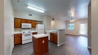 This single-story residence is thoughtfully designed with a functional, open-concept layout that connects the kitchen and living areas seamlessly. The kitchen is well-equipped with warm-toned wood cabinetry, white appliances including a range, over-the-range microwave, refrigerator, and dishwasher, complemented by speckled countertops and a central island that provides additional prep space. Wood-look plank flooring runs throughout the kitchen and living areas, adding durability and visual continuity.

The living area is generously sized, featuring a ceiling fan with integrated lighting and a window that allows natural light to brighten the space. A secondary view from the living area reveals a hallway leading to the private quarters of the home.

The bedrooms are carpeted for comfort and each features a ceiling fan with lighting and windows with blinds. At least one bedroom includes access to a walk-in closet with shelving, offering practical storage solutions.

The bathrooms are finished with wood-look flooring, warm wood vanity cabinetry, speckled countertops, and single-sink vanities. One bathroom includes a tub-shower combination with tiled surround, while the other is configured as a three-quarter bath. The overall ambiance of the space is neutral and move-in ready.