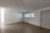Located at 8601 Roberts Dr in Sandy Springs, GA, this one-bedroom, one-bathroom unit offers a well-organized single-floor layout with a practical mix of living spaces. The living room is generously sized, featuring durable wood-look laminate flooring, crisp white walls, a textured ceiling, and a wide window that invites natural light and views of surrounding greenery. The space flows into the kitchen, which is laid out in a galley configuration with dark cabinetry, granite-style countertops, and light tile flooring — providing ample prep and storage space. A pendant light fixture adds a functional accent over the passage connecting to the living area. The bedroom offers a comfortable footprint with plush carpeting, neutral walls, and a sliding glass door that opens to an outdoor balcony or patio with wooded views. An adjacent closet provides dedicated storage. The hallway connects the main living areas to the full bathroom, which features a dark vanity with a granite-topped sink, a large mirror, wood-look flooring, and a tiled shower/tub combination. Throughout the unit, the consistent use of neutral tones and updated finishes creates a clean, cohesive atmosphere suited to everyday living.