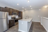 This single-floor residence offers a thoughtfully designed layout with contemporary finishes throughout. The kitchen serves as a central highlight, featuring dark espresso cabinetry, stainless steel appliances including a refrigerator, range, and microwave, and a spacious island topped with light granite countertops and an integrated sink. Wood-look flooring runs through the kitchen and main living areas, contributing to a cohesive, modern aesthetic. Recessed lighting illuminates the kitchen, enhancing its clean, open feel.

A staircase with a white-capped half-wall railing connects to the upper-level landing, which opens to carpeted living areas bathed in natural light from large windows. The bedrooms are generously sized, each featuring plush carpet, neutral gray walls, and ceiling fans. The primary bedroom showcases a tray ceiling detail that adds architectural character.

The primary bathroom is well-appointed with a granite-topped vanity, dark cabinetry, a large framed mirror, and wood-look flooring. It connects directly to a walk-in closet lined with white shelving systems and hanging rods, providing ample storage. Throughout the residence, neutral tones and consistent finishes create a clean, move-in-ready atmosphere.