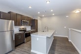 This single-floor residence offers a thoughtfully designed layout with contemporary finishes throughout. The kitchen serves as a central highlight, featuring dark espresso cabinetry, stainless steel appliances including a refrigerator, range, and microwave, and a spacious island topped with light granite countertops and an integrated sink. Wood-look flooring runs through the kitchen and main living areas, contributing to a cohesive, modern aesthetic. Recessed lighting illuminates the kitchen, enhancing its clean, open feel.

A staircase with a white-capped half-wall railing connects to the upper-level landing, which opens to carpeted living areas bathed in natural light from large windows. The bedrooms are generously sized, each featuring plush carpet, neutral gray walls, and ceiling fans. The primary bedroom showcases a tray ceiling detail that adds architectural character.

The primary bathroom is well-appointed with a granite-topped vanity, dark cabinetry, a large framed mirror, and wood-look flooring. It connects directly to a walk-in closet lined with white shelving systems and hanging rods, providing ample storage. Throughout the residence, neutral tones and consistent finishes create a clean, move-in-ready atmosphere.