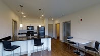 This 2-bedroom, 2.5-bathroom residence is designed with a modern aesthetic and thoughtfully arranged across a single floor. The open-concept living area seamlessly connects the kitchen and dining space, creating a cohesive and functional layout ideal for everyday living and entertaining.

The kitchen is a standout feature, outfitted with crisp white cabinetry, dark granite countertops, and black appliances including a refrigerator, range, and microwave. A central island with seating provides additional prep space and casual dining options, illuminated by sleek pendant lighting above. Recessed lighting throughout ensures the space is well-lit and inviting.

Rich, dark hardwood-style flooring runs throughout the main living area, offering a warm contrast to the light-toned walls and white cabinetry. The dining area adjacent to the kitchen accommodates a table and chairs, making it a practical space for shared meals.

The residence includes two well-appointed bedrooms, each with access to their own bathroom, plus an additional half bath for guests. Clean architectural lines, neutral tones, and quality finishes contribute to a polished, contemporary ambiance that is both functional and visually appealing throughout the home.