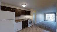 This single-floor residence offers a practical and functional layout designed for comfortable everyday living. The kitchen is a standout area, featuring dark espresso-toned wood cabinetry that provides ample storage space, complemented by granite-look countertops and a stainless steel sink. White appliances — including a gas range, dishwasher, and refrigerator — are seamlessly integrated into the design, creating a clean and cohesive look. The flooring in the kitchen consists of light-toned vinyl tile, offering easy maintenance and durability. The kitchen opens directly into an adjacent living area, which is finished with wall-to-wall carpeting in a neutral tone, lending a cozy and comfortable atmosphere to the space. The transition between these two areas creates a natural flow suited for daily living. Walls throughout are painted in soft, neutral tones, contributing to a bright and welcoming ambiance. A flush-mount ceiling light in the kitchen provides reliable overhead illumination. The overall design is straightforward and practical, prioritizing functionality while maintaining a clean, well-organized aesthetic throughout the unit.