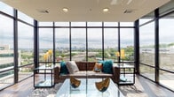 This contemporary high-rise residence delivers a striking first impression through its expansive floor-to-ceiling window walls in the open-concept living and dining area. The wall of glass frames panoramic city skyline views, flooding the space with natural light and creating a seamless connection between the interior and the urban landscape beyond. Rich hardwood flooring flows throughout, anchoring the modern aesthetic.

The living area is anchored by a tufted leather sofa, a sculptural glass coffee table, and elegant brass floor lamps, all arranged to maximize the dramatic views. Adjacent to the living space, the dining area accommodates a glass-top table with bold yellow accent chairs, positioned to enjoy the same sweeping vistas.

The chef-inspired kitchen is outfitted with crisp white cabinetry, a subway tile backsplash, quartz countertops, stainless steel appliances, a center island with bar seating, and pendant lighting overhead — combining function with refined style.

The primary bedroom offers a serene retreat with warm neutral tones, soft carpeting, and direct access to an en-suite bathroom featuring a floating vanity, wood-toned cabinetry, and contemporary fixtures. A second well-appointed bedroom and an additional full bathroom with similar finishes complete the layout, delivering a cohesive and polished living experience throughout.