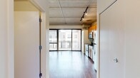 Located at 618 S Main St in Ann Arbor, MI, this urban studio offers an efficient, well-designed layout with a distinct industrial-loft aesthetic. The open living area is defined by exposed concrete ceilings with visible conduit and ductwork, complemented by adjustable track lighting that provides both functionality and character. Warm hardwood flooring runs throughout, creating a cohesive and inviting atmosphere. Floor-to-ceiling sliding glass doors flood the main living space with natural light while offering views of the surrounding cityscape, reinforcing the urban character of the unit. The kitchen is thoughtfully appointed with warm honey-toned cabinetry, dark granite countertops, and a full suite of stainless steel appliances including a range, microwave, dishwasher, and refrigerator. A wine rack accent adds a stylish touch to the upper cabinetry. The bathroom features tile-surround walk-in shower, a wood-toned vanity with dark countertop, and a large mirror. Exposed concrete walls in the living area contribute to the raw, loft-inspired character of the space. Situated in the heart of Ann Arbor's vibrant South Main corridor, this studio is ideal for those seeking a modern, urban lifestyle with easy access to local dining, entertainment, and the University of Michigan campus.