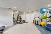 Located at 8365 Dix Ellis Trail in Jacksonville, FL, this fitness center is a thoughtfully designed, single-floor facility that offers a comprehensive workout environment. The space is organized into distinct functional zones, each catering to different aspects of physical training.

The main workout area features speckle-finish flooring and is anchored by a row of treadmills positioned beneath windows that allow natural light to filter in. An artistic geometric line-art mural adorns the wall, adding a dynamic visual element to the cardio zone. Adjacent to this area is a free weights section with a full rack of dumbbells and adjustable benches, all reflected in a large wall mirror that enhances the sense of space.

A separate zone with blue-toned flooring houses a dedicated rack of stability and functional training equipment, including colorful exercise balls, resistance bands, foam rollers, and medicine balls. A massage chair and a water station provide recovery and hydration amenities, completing the wellness-focused setup.

A distinct ancillary room features warm hardwood-style flooring and a bold tropical botanical wallpaper mural, creating an inviting atmosphere for yoga, stretching, or mind-body training. This room also includes a smart fitness mirror and a BOSU balance trainer, with a window offering a glimpse of the surrounding greenery.

Throughout, recessed lighting and a clean white-and-blue palette create a bright, modern, and motivating environment.