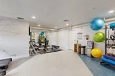 Located at 8365 Dix Ellis Trail in Jacksonville, FL, this fitness center is a thoughtfully designed, single-floor facility that offers a comprehensive workout environment. The space is organized into distinct functional zones, each catering to different aspects of physical training.

The main workout area features speckle-finish flooring and is anchored by a row of treadmills positioned beneath windows that allow natural light to filter in. An artistic geometric line-art mural adorns the wall, adding a dynamic visual element to the cardio zone. Adjacent to this area is a free weights section with a full rack of dumbbells and adjustable benches, all reflected in a large wall mirror that enhances the sense of space.

A separate zone with blue-toned flooring houses a dedicated rack of stability and functional training equipment, including colorful exercise balls, resistance bands, foam rollers, and medicine balls. A massage chair and a water station provide recovery and hydration amenities, completing the wellness-focused setup.

A distinct ancillary room features warm hardwood-style flooring and a bold tropical botanical wallpaper mural, creating an inviting atmosphere for yoga, stretching, or mind-body training. This room also includes a smart fitness mirror and a BOSU balance trainer, with a window offering a glimpse of the surrounding greenery.

Throughout, recessed lighting and a clean white-and-blue palette create a bright, modern, and motivating environment.