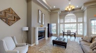 Located at 301 Converse Center St in Converse, Texas, this single-story community space presents an impressive architectural design anchored by a striking rotunda-style entry hall. The foyer is defined by a ring of tall, classical white columns rising to soaring ceilings, with clerestory windows encircling the upper rotunda to flood the space with natural light. Decorative tile flooring with inlaid mosaic border detailing adds a refined touch underfoot throughout the entry.

Beyond the foyer, the main lounge area offers a warm and inviting atmosphere with high tray ceilings accented by crown molding and an elegant chandelier. A classic white fireplace with tile surround serves as a focal point, flanked by generous wall space ideal for artwork. Large arched windows and glass-panel doors bathe the room in natural light while offering views to the outdoors.

The lounge flows seamlessly into a dining area and an open-concept kitchen, separated by a column-framed peninsula with dark countertops and pendant lighting. The kitchen is equipped with white cabinetry, stainless steel appliances, and ample counter space. Additional corridor spaces provide quiet seating nooks, and the overall neutral color palette of warm taupes and crisp whites contributes to an atmosphere that is both welcoming and sophisticated throughout.