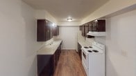 This single-floor unit offers a practical and functional layout with distinct living, kitchen, and bedroom spaces. The galley-style kitchen is well-appointed with rich, dark wood cabinetry on both sides, light-toned countertops, a double sink, and white appliances including a coil-burner range and refrigerator. Wood-look flooring runs throughout the kitchen, adding warmth and durability to the space.

The living area is generously proportioned, featuring neutral carpet and an open connection to the kitchen, creating a cohesive flow between the main living and dining spaces. A closet off the living area provides convenient built-in storage.

The bedrooms are finished with soft, neutral carpet and feature textured ceilings throughout. Each room is fitted with window blinds that allow for natural light while maintaining privacy. One bedroom includes a ceiling fan with a light fixture, while another offers a closet with sliding doors. The windows in the bedrooms frame views of the surrounding outdoor environment, bringing a sense of connection to the exterior.

Overall, the unit presents a clean, straightforward design with consistent finishes across all rooms, offering a comfortable and move-in-ready living environment.