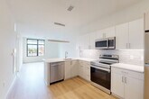 Located at 2 West 4th Street in downtown Wilmington, Delaware, this one-bedroom, one-bathroom unit offers a thoughtfully designed open-concept layout with modern finishes throughout. Light hardwood flooring flows seamlessly across the entire space, creating a warm, cohesive aesthetic.

The kitchen is a standout feature, showcasing crisp white cabinetry, white subway tile backsplash, and a full suite of stainless steel appliances including a range, microwave, dishwasher, and refrigerator. A peninsula with a white quartz countertop and undermount sink adds both prep space and a natural division between the kitchen and the adjacent dining and living areas. Pendant lighting above the peninsula enhances the modern feel. Large, black-framed windows allow generous natural light to fill the open living area.

The bedroom is a well-proportioned, serene retreat with a large black-framed window offering views of the surrounding Wilmington streetscape. Two closets provide ample storage throughout the unit. The bathroom features a clean, minimalist design with a tub-shower combo clad in white tile, a vanity with storage, and recessed lighting. An in-unit laundry area adds everyday convenience to this well-appointed urban residence.