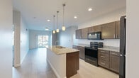 Located at 2540 Promenade Way in Portage, Indiana, this well-appointed 2-bedroom, 1-bathroom residence offers a thoughtfully designed single-floor layout with modern finishes throughout. The open-concept kitchen and living area serves as the heart of the home, featuring rich dark cabinetry, granite countertops, a central island with pendant lighting, black appliances, and light wood-style flooring that extends into the living room. Sliding glass doors lead from the living area to a private balcony overlooking the landscaped community grounds, offering pleasant outdoor views. The spacious primary bedroom is carpeted and includes access to a dedicated closet with wire shelving, providing ample storage. The second bedroom also features carpet flooring and a window with exterior views, filling the room with natural light. The bathroom is finished with a dark vanity cabinet, granite countertop, and a large mirror. A dedicated laundry area houses a full-size washer and dryer, adding convenience to daily living. Neutral wall tones, recessed lighting, and consistent finishes tie the space together, creating a clean, modern, and comfortable living environment throughout.