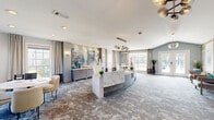 Located at 14801 Lemoyne Blvd in Biloxi, Mississippi, this thoughtfully designed single-floor reception space offers a refined and welcoming atmosphere through a seamless blend of contemporary design elements. The centerpiece of the room is a striking curved reception desk clad in richly veined white marble, lending an air of sophistication and professionalism to the space.

Overhead, a dramatic mid-century modern chandelier featuring clustered globe pendants in smoked and metallic finishes anchors the room and draws the eye upward to the clean white ceiling. The flooring is covered in an artistically patterned carpet in cool grey and blue tones, adding visual depth and texture underfoot.

A textured wood-paneled accent wall serves as a bold architectural backdrop, displaying two large-scale abstract artworks with oceanic blue hues that complement the room's cool, coastal palette. Flanking seating areas feature plush, contemporary lounge chairs and a small café-style table, creating comfortable spaces for conversation or waiting.

Natural light filters in through multiple windows dressed with flowing linen drapes, and French doors open to the outdoors, connecting the interior to the surrounding environment. Private offices with frosted glass doors are accessible from the main area, balancing openness with functionality. The overall ambiance is polished, airy, and modern.