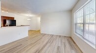 Located at 1475 Wilton Farm Road in Charlottesville, Virginia, this two-bedroom, one-bathroom single-floor residence offers a practical and well-organized layout. The living room is bright and open, featuring light wood-style flooring, neutral white walls, and a large window that brings in generous natural light and outdoor views. An adjacent dining area flows naturally into the galley-style kitchen, which is equipped with warm wood cabinetry, granite-look countertops, a stainless steel refrigerator, stove, and dishwasher, all illuminated by track lighting overhead. A textured ceiling is present throughout the common areas, adding subtle architectural detail. Both bedrooms are comfortably sized, each with windows providing natural light. The primary bedroom features light wood-style flooring, while the secondary bedroom is finished with plush carpet for added comfort. The full bathroom includes a clean white tub-shower combination and a vanity with ample mirror space. A dedicated laundry room with hookups and wire shelving above adds everyday convenience. Two closets and a utility room provide practical storage solutions throughout. The overall aesthetic is clean, neutral, and move-in ready.