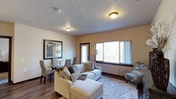 Located at 1605 North River Ridge Boulevard in Spokane, WA, this single-floor residence offers a well-designed layout with a cohesive, neutral color palette throughout. The open-concept living and dining area is bright and welcoming, featuring dark hardwood-style flooring, a textured ceiling, and large windows that invite natural light and offer views of the surrounding greenery. A private exterior door in the living area provides convenient outdoor access.

The kitchen is a functional centerpiece, outfitted with rich dark cabinetry, granite-style countertops, stainless steel appliances including a range, microwave, and refrigerator, and a peninsula bar with seating for two. Track lighting and pendant lights illuminate the workspace effectively.

Two well-proportioned bedrooms offer carpeted floors and natural light. The primary bedroom includes a walk-in closet with wire shelving, while the second bedroom features a standard sliding closet. Both rooms provide a calm, restful ambiance.

Two bathrooms serve the space: one with a walk-in shower and tile flooring, the other with a shower/tub combination, both finished with dark wood vanities and granite-style counters. A dedicated in-unit laundry area accommodates a full-size washer and dryer with overhead shelving for added storage.
