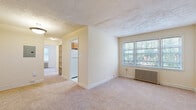 Located at 853 21st St NE, Unit 8 in Washington, DC, this one-bedroom, one-bathroom unit offers a practical and well-organized layout. The living area features soft carpet flooring, neutral cream-toned walls, and a textured ceiling, creating a warm and understated ambiance. A large window allows ample natural light to fill the space, complemented by a classic cast-iron radiator that provides reliable warmth. The kitchen is efficiently designed, featuring wood-toned cabinetry and a full-size refrigerator, with built-in shelving nearby offering additional storage. The bedroom is a comfortably sized retreat with two windows that invite natural light and views of surrounding greenery. A cast-iron radiator adds to the room's cozy character, while carpet underfoot keeps the atmosphere inviting. The bathroom is clean and functional, featuring a full-size tub and shower combination with white tile surround, a window for natural ventilation, and straightforward fixtures. A connecting hallway ties the rooms together seamlessly, providing easy flow throughout the unit. The overall design is simple and practical, making it a solid Washington, DC address with essential amenities in a compact, efficient footprint.