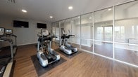 Located at 300 Hickory Hollow Pl in Nashville, Tennessee, this single-floor fitness center is thoughtfully designed to support a well-rounded cardio workout experience. The space is defined by its sleek, modern aesthetic, centered around floor-to-ceiling glass partition walls framed in aluminum, which create an open, airy atmosphere while visually expanding the room. Natural light filters in through large windows along the perimeter, complementing the recessed ceiling lighting throughout.

The fitness center is equipped with a comprehensive selection of True-brand cardio machines, including treadmills, upright and recumbent stationary bikes, and elliptical cross-trainers — all positioned on protective rubber mats atop warm hardwood-style flooring. Wall-mounted flat-screen televisions provide entertainment options for users on the treadmills and bikes, enhancing the workout experience. The neutral gray walls and clean white trim contribute to a bright, motivating environment.

The layout is efficiently organized, with distinct zones separating machine types while maintaining an unobstructed flow throughout the space. A glass-paned entrance door connects the fitness area to adjacent spaces, reinforcing the open, transparent design language found throughout. The overall ambiance is clean, modern, and purpose-built — offering residents a well-equipped facility for their daily fitness routines.
