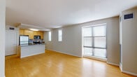This single-floor residence is designed with an open, functional layout that promotes a seamless flow between the kitchen and living areas. The kitchen serves as a central feature, anchored by a large island with a granite countertop and integrated sink, offering both additional prep space and a natural gathering point. Light wood cabinetry provides ample storage, while stainless steel appliances—including a refrigerator, microwave, and range—are complemented by a striking herringbone-patterned tile backsplash. Granite counters extend throughout the kitchen workspace, adding a polished finish.

The open living area is finished with warm hardwood-style flooring that runs consistently throughout the unit, creating a cohesive aesthetic. Multiple windows fitted with horizontal blinds allow natural light to fill the space generously. The bedroom includes a walk-in closet with built-in shelving and rod systems, providing organized storage. The bathroom features a walk-in shower finished with classic white subway tile and a contrasting gray accent band, chrome fixtures, and a clean, contemporary design. Neutral wall tones throughout contribute to a bright, versatile atmosphere.