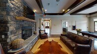 Located at 756 Twin Willow Dr in Rock Hill, SC, this single-story space is designed with a rustic-modern aesthetic that balances comfort and style throughout. The focal point of the main living area is a striking floor-to-ceiling stacked stone fireplace, complete with a reclaimed wood mantel and a wall-mounted television above, creating an inviting atmosphere for gatherings. Rich leather seating and layered rugs, including a cowhide accent over a natural fiber base, add texture and warmth to the space.

Architectural interest is provided by tray ceilings accented with dark wood beams and recessed lighting, adding depth and a refined character to the interior. Polished concrete floors flow throughout, offering both durability and a cohesive visual continuity between areas.

The kitchen is outfitted with rich dark wood cabinetry, granite-style countertops, and stainless steel appliances, including an electric range and over-the-range microwave. A pass-through connects the kitchen to adjacent spaces, enhancing the open feel of the layout.

A dedicated dining area features high-top tables with reclaimed wood chairs positioned near a window offering views of the outdoor surroundings. Additional rooms visible in the layout suggest flexible spaces suitable for varied uses. Overall, the space presents a cohesive, well-appointed environment with character-rich details throughout.