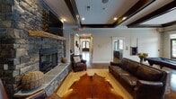 Located at 756 Twin Willow Dr in Rock Hill, SC, this single-story space is designed with a rustic-modern aesthetic that balances comfort and style throughout. The focal point of the main living area is a striking floor-to-ceiling stacked stone fireplace, complete with a reclaimed wood mantel and a wall-mounted television above, creating an inviting atmosphere for gatherings. Rich leather seating and layered rugs, including a cowhide accent over a natural fiber base, add texture and warmth to the space.

Architectural interest is provided by tray ceilings accented with dark wood beams and recessed lighting, adding depth and a refined character to the interior. Polished concrete floors flow throughout, offering both durability and a cohesive visual continuity between areas.

The kitchen is outfitted with rich dark wood cabinetry, granite-style countertops, and stainless steel appliances, including an electric range and over-the-range microwave. A pass-through connects the kitchen to adjacent spaces, enhancing the open feel of the layout.

A dedicated dining area features high-top tables with reclaimed wood chairs positioned near a window offering views of the outdoor surroundings. Additional rooms visible in the layout suggest flexible spaces suitable for varied uses. Overall, the space presents a cohesive, well-appointed environment with character-rich details throughout.