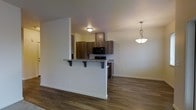 This single-floor space offers a thoughtfully designed open-concept layout that seamlessly connects the kitchen and living areas. The kitchen is a standout feature, outfitted with rich dark wood cabinetry that provides ample storage, granite-look countertops, and black appliances including a built-in microwave. A raised peninsula with bar-height seating serves as both a functional workspace and a casual dining spot, elegantly separating the kitchen from the adjacent living area. A stylish pendant light with a brushed nickel finish hangs above the dining zone, adding a decorative focal point to the space. Throughout the unit, dark hardwood flooring runs continuously, lending warmth, cohesion, and a modern aesthetic. The walls are finished in a clean, neutral tone that enhances the sense of brightness and openness. Flush-mounted ceiling lighting in the kitchen ensures practical illumination, while the overall layout promotes an easy flow between functional zones. The clean lines, contemporary fixtures, and durable finishes come together to create a space that is both practical and visually appealing — well-suited for everyday living and entertaining alike.