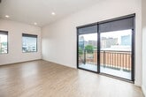 This contemporary urban unit offers a thoughtfully designed single-floor layout with a clean, modern aesthetic. The open living area is bright and airy, featuring light wood-tone flooring, recessed lighting, and crisp white walls that maximize the sense of space. Large black-framed sliding glass doors lead to a private balcony, offering sweeping views of the surrounding cityscape, while an additional window fills the room with natural light. An exposed metallic ductwork detail adds an industrial character to the soaring ceiling height in the main living space.

The kitchen is well-appointed with dark wood cabinetry, white subway tile backsplash, white quartz countertops, and a full suite of stainless steel appliances including a refrigerator, range, microwave, and dishwasher. A dedicated in-unit laundry closet with a stacked washer and dryer provides added convenience. A built-in desk or counter nook offers a functional workspace seamlessly integrated into the layout.

The bathroom features warm wood-tone flooring consistent with the rest of the unit, a dark wood vanity with a white countertop, a well-lit mirror, and a walk-in shower. Throughout the space, the design balances modern industrial touches with clean, comfortable finishes, creating a stylish and functional urban living environment.