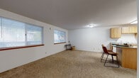 This single-floor unit offers a practical and straightforward layout, designed to maximize usable living space across several distinct areas. The spacious living room is finished with neutral wall-to-wall carpeting and features multiple windows dressed with horizontal blinds, allowing natural light to filter in while providing views of the surrounding outdoors. A pet door is also present in this main living area. The space is versatile and generously sized, lending itself well to a variety of furniture arrangements.

The kitchen is equipped with warm oak cabinetry — both upper and lower — paired with distinctive teal laminate countertops that add a retro character to the space. Tile flooring runs throughout the kitchen, and the room includes a dishwasher, electric range, microwave, and a central island with matching cabinetry and countertop, providing additional prep and storage space.

The bedrooms are carpeted and bright, each featuring windows with blinds and baseboard heating units. The full bathroom includes a tub-shower combination, toilet, and an oak vanity with a teal countertop and sink, consistent with the kitchen's design palette. Tile flooring and a sliding door complete the bathroom. Overall, the unit presents a cohesive, functional design throughout.