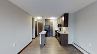 This single-floor unit offers a thoughtfully designed layout with a cohesive, neutral color palette that creates a calm and inviting atmosphere throughout. The kitchen is a standout feature, showcasing rich dark wood cabinetry that extends to the ceiling for maximum storage, complemented by a light-toned countertop, tile backsplash, and black appliances including a refrigerator, range, and microwave. A peninsula provides additional prep space and casual seating, while hardwood-style flooring ties the kitchen and adjacent areas together seamlessly. The living area is generously proportioned, featuring the same hardwood-style flooring, soft grey walls, and a large window that draws in natural light. Baseboard heating runs along the perimeter walls, a practical and efficient feature consistent throughout the unit. The bedroom is carpeted for comfort, with grey walls, a window for natural light, and baseboard heating. The bathroom is finished with a classic pedestal sink, a mirrored medicine cabinet, a shower with a curtain enclosure, and warm wood-look flooring. A three-bulb vanity light provides bright, even illumination. Overall, the unit balances modern finishes with functional design for comfortable everyday living.