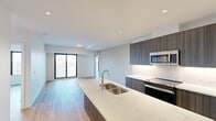 Located at 66 Weber St E in Kitchener, Ontario, this modern three-bedroom, two-bathroom unit offers a thoughtfully designed open-concept layout. The living and kitchen areas flow seamlessly together, creating a bright, cohesive space anchored by a large waterfall-edge quartz island with an undermount double sink. The kitchen is equipped with stainless steel appliances, including a refrigerator, stove, built-in microwave, and dishwasher, complemented by tall dark wood cabinetry with under-cabinet lighting and a clean white tile backsplash. Light-toned hardwood flooring runs throughout the unit, contributing to an airy, contemporary feel. Sliding glass doors in the living area invite natural light and provide access to outdoor views. Each bedroom features neutral walls, light flooring, and double closets with classic panel doors and matte black hardware. The primary bedroom is accompanied by a sleek ensuite bathroom complete with a glass-enclosed shower, quartz vanity, and modern fixtures. A second full bathroom includes a soaker tub with full-height white tile surround and a matching quartz vanity. The overall design is clean, minimalist, and move-in ready.