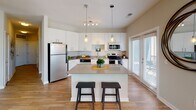 Located at 5834 White Lake Lane in Frederick, MD, this thoughtfully designed apartment offers a contemporary living experience across a single floor. The open-concept kitchen is a standout feature, showcasing white cabinetry, stainless steel appliances including a refrigerator, electric range, and microwave, complemented by a large center island with pendant lighting and a quartz-style countertop — ideal for both cooking and casual dining. Wood-look flooring flows through the kitchen and adjoining areas, while a glass door provides direct access to an outdoor space. The living area is bright and welcoming, featuring large windows with horizontal blinds that flood the room with natural light, a ceiling fan, and an open layout that accommodates both a lounge and a dedicated workspace with built-in shelving. The bedrooms are carpeted and comfortably scaled, each with windows offering outdoor views and ceiling fans for comfort. Two bathrooms serve the unit: one features a soaking tub and shower combination with wood-look flooring and white cabinetry, while the primary bathroom offers a walk-in glass shower, dual-sink vanity, and warm wood-look floors. Neutral tones throughout create a clean, modern ambiance.
