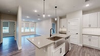 This single-floor residence showcases a thoughtfully designed open-concept layout with consistent modern finishes throughout. The kitchen serves as a central feature, equipped with white shaker-style cabinetry accented by matte black hardware, light quartz countertops, a classic subway tile backsplash, and a full suite of stainless steel appliances including a range, over-the-range microwave, and dishwasher. A generously sized center island with an undermount sink and pendant lighting above connects seamlessly to the living area, which benefits from natural light through large windows fitted with roller shades.

The bedrooms feature wood-look plank flooring, neutral-toned walls, and windows overlooking the surrounding neighborhood landscape. The primary bathroom includes a walk-in glass-door shower, white vanity cabinetry with quartz countertops, and a lighted mirror, while an adjoining walk-in closet provides organized storage. A secondary full bathroom offers a soaking tub, single-sink vanity with matching finishes, and matte black fixtures throughout.

The attached garage provides a spacious, clean concrete-floored area with an automatic opener. Consistent wood-look flooring, recessed lighting, and a neutral color palette unify the home's overall aesthetic.