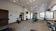 Located at 18417 E Appleway Ave in Spokane Valley, WA, this single-level fitness center is designed to support a comprehensive workout experience. The space features soaring vaulted ceilings with recessed lighting, neutral-toned walls, and durable patterned carpet flooring throughout, creating a clean and functional environment.

The facility is generously outfitted with a wide variety of equipment to accommodate diverse fitness routines. Cardio options include a True treadmill, a Peloton stationary bike, an elliptical trainer, and a WaterRower rowing machine. For strength training, the space includes a multi-station cable machine, a full dumbbell rack, a weight bench, and an assortment of medicine balls and TRX suspension training equipment.

A standout architectural feature is the full-width glass garage door on one wall, which opens completely to an adjacent outdoor area, allowing natural light and fresh air to flow into the space during workouts. Additional windows along the perimeter further enhance natural light. Wall-mounted flat-screen televisions are positioned throughout for entertainment during exercise sessions.

The fitness center also includes a restroom, providing added convenience for users. The warm wood trim accents around doors and windows add a refined touch to the otherwise utilitarian design, resulting in a space that is both practical and inviting.