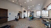 Located at 18417 E Appleway Ave in Spokane Valley, WA, this single-level fitness center is designed to support a comprehensive workout experience. The space features soaring vaulted ceilings with recessed lighting, neutral-toned walls, and durable patterned carpet flooring throughout, creating a clean and functional environment.

The facility is generously outfitted with a wide variety of equipment to accommodate diverse fitness routines. Cardio options include a True treadmill, a Peloton stationary bike, an elliptical trainer, and a WaterRower rowing machine. For strength training, the space includes a multi-station cable machine, a full dumbbell rack, a weight bench, and an assortment of medicine balls and TRX suspension training equipment.

A standout architectural feature is the full-width glass garage door on one wall, which opens completely to an adjacent outdoor area, allowing natural light and fresh air to flow into the space during workouts. Additional windows along the perimeter further enhance natural light. Wall-mounted flat-screen televisions are positioned throughout for entertainment during exercise sessions.

The fitness center also includes a restroom, providing added convenience for users. The warm wood trim accents around doors and windows add a refined touch to the otherwise utilitarian design, resulting in a space that is both practical and inviting.