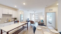 This single-floor residence offers a thoughtfully designed open-concept layout that seamlessly connects the kitchen, dining, and living areas. Light wood-style flooring flows throughout the main living spaces, creating a cohesive and contemporary aesthetic. The kitchen is a standout feature, equipped with stainless steel appliances, white shaker-style cabinetry extending to the ceiling, granite countertops, a tile backsplash, and a large island with seating — ideal for both meal preparation and casual dining.

The living area is bright and airy, benefiting from natural light streaming through oversized windows and a glass-paneled door. A ceiling fan provides additional comfort overhead. The open dining space adjacent to the kitchen accommodates a full dining setup.

The unit includes two carpeted bedrooms, each comfortably sized with ample natural light and neutral finishes. The primary bedroom connects to an en-suite bathroom featuring a glass-enclosed shower, granite vanity, hardwood-style flooring, and direct access to a spacious walk-in closet outfitted with wire shelving and hanging rods. The overall ambiance throughout is clean, modern, and move-in ready.