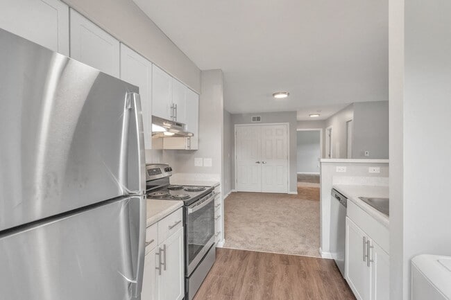 Open-concept living with hardwood kitchen floors flowing into the carpeted living room, stainless steel appliances, and abundant natural light, professionally managed by Highlands Vista Group. - Arbor Crossings