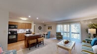This thoughtfully designed single-floor residence offers two bedrooms and two bathrooms within a comfortable and functional layout. The open-concept living, dining, and kitchen area forms the heart of the home, bathed in natural light streaming through large sliding glass doors fitted with vertical blinds that lead to outdoor views of lush greenery. The living area features plush carpeting and ample space for seating arrangements.

The kitchen is well-equipped with warm honey-toned cabinetry, granite countertops, a decorative tile backsplash, and black appliances including a refrigerator, range, microwave, and dishwasher. A central breakfast bar with seating connects the kitchen seamlessly to the dining area, making it ideal for both casual meals and entertaining.

The spacious primary bedroom offers a tranquil retreat with soft carpet, generous wall space, and direct access to a walk-in closet. The second bedroom is equally comfortable, featuring carpet flooring and a window with outdoor views. Both bathrooms are functional and clean, with one featuring a full tub-shower combination with tiled flooring. A hallway and dedicated closet provide additional storage throughout the residence.