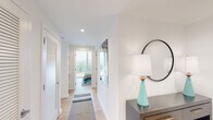 This contemporary single-floor residence showcases a clean, modern aesthetic throughout, with crisp white walls, light hardwood flooring, and an abundance of natural light streaming through expansive floor-to-ceiling windows. The open-concept living area is bright and airy, offering sweeping treetop and cityscape views that serve as a stunning backdrop to everyday living. A dedicated workspace nook sits beside the windows, making the most of the natural light and scenery.

The kitchen is well-equipped and thoughtfully designed, featuring two-tone cabinetry — warm wood uppers paired with slate-blue lowers — stainless steel appliances, a white subway tile backsplash, and a generous quartz-topped island with seating for multiple guests, ideal for both casual dining and entertaining.

A hallway lined with louvered closet doors connects the living spaces to the bedrooms. The primary bedroom is generously sized with dual floor-to-ceiling windows framing lush treetop views, while a second bedroom enjoys a large window with striking city and landmark views. Both rooms are serene and filled with natural light.

The bathrooms are distinctly styled: one features a sleek grey vanity with backlit mirrors, while the other offers a full glass-enclosed walk-in shower with stone-look tile. Throughout, the space maintains a cohesive modern sensibility with refined finishes and thoughtful design details.
