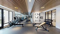 Located at 2480 First St in Fort Myers, Florida, this fitness center offers a generously sized, single-floor layout designed to accommodate a comprehensive workout experience. The space is defined by its striking architectural detail — a continuous wood-slat ceiling that runs throughout the main workout area, lending warmth and a modern aesthetic to the facility. Durable rubber flooring provides both safety and comfort underfoot across all zones.

The cardio section is well-appointed with a full row of treadmills, elliptical trainers, stationary bikes, rowing machines, and a stair climber with an integrated digital display. A dedicated cycling studio houses multiple spin bikes alongside floor-to-ceiling mirrors and direct access to natural light through large glass doors. An adjacent strength training area features a multi-station cable machine, adjustable benches, dumbbells on organized racks, and a variety of weight plates and bars.

Large floor-to-ceiling windows and glass doors flood the space with natural light and offer views of the surrounding outdoor greenery. Ceiling fans are positioned throughout to maintain airflow. A motivational "One More Rep" wall graphic serves as a bold focal point, reinforcing the facility's energetic atmosphere. Wall-mounted televisions add convenience for users during extended workout sessions.