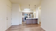 This single-story residence offers a practical and modern layout across three bedrooms and three full bathrooms. The open-concept kitchen serves as the heart of the home, featuring a large island with a striking white quartz countertop, an undermount sink, and stainless steel appliances including a refrigerator, range, and microwave. Warm taupe cabinetry provides ample storage, while pendant lighting adds a contemporary touch. A convenient in-unit laundry area with washer and dryer is tucked adjacent to the kitchen. Light wood-look flooring flows throughout the main living areas, creating a cohesive and easy-to-maintain surface. The living room is bright and airy, benefiting from large windows and glass doors that invite natural light and provide views of the outdoors. A wall-mounted HVAC unit ensures year-round comfort. The three bedrooms are carpeted for warmth and comfort, each featuring neutral tones and windows that allow natural light. The primary bedroom offers a generous footprint well-suited to a full furniture arrangement. Each of the three bathrooms is finished with wood-look flooring, a tub-shower combination, and a single-sink vanity with clean white countertops. Two hallways connect the spaces efficiently, contributing to the home's functional and well-organized flow.