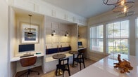 Located at 15270 Voss Rd in Sugar Land, Texas, this single-floor business center is a thoughtfully designed professional workspace that blends functionality with refined aesthetics. The space is entered through glass-paneled doors that offer a preview of the bright, welcoming interior, finished with elegant crown molding and light herringbone-patterned hardwood flooring throughout.

The main workspace features dedicated computer workstations along the perimeter walls, each equipped with monitors and ample desk surface, complemented by warm task lighting and leather-accented wall-mounted sconces. A built-in banquette nook with navy blue cushioned seating and a paneled accent wall provides a comfortable and semi-private area for focused work or informal meetings. Paired with sleek black café-style chairs and dark marble-top bistro tables, this nook is both stylish and practical.

A secondary area houses a printer station with built-in cabinetry in a muted sage-gray finish, additional counter workspace, and a large chalkboard panel. Interior windows connect the space visually to adjacent common areas, maintaining an open, connected feel. Multiple windows fitted with slatted blinds allow generous natural light to fill the room while providing adjustable privacy. The overall ambiance is clean, modern, and professional, making this business center a well-equipped resource for productivity.