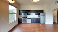 This single-floor 2-bedroom, 1-bathroom residence offers a thoughtfully designed layout that balances comfort and functionality. The open living and dining area is highlighted by rich hardwood-style flooring, a ceiling fan with light fixture, and an elegant pendant light. Large sliding glass doors lead to a private balcony with decorative iron railings, filling the space with natural light and outdoor views. An additional window further brightens the area.

The kitchen features dark espresso cabinetry with granite-style countertops, ample upper and lower storage, and a full suite of stainless steel appliances including a refrigerator, electric range, microwave, and dishwasher. A window above the sink adds natural light to the workspace.

Both bedrooms are carpeted and bathed in natural light through well-sized windows offering views of the surrounding landscape. The rooms provide a calm, neutral palette ideal for personalization.

The bathroom is finished with matching dark cabinetry, a granite-topped vanity with a square undermount sink, a stylish three-bulb vanity light fixture, a large mirror, and a shower-tub combination with glass enclosure. Wood-style flooring ties the bathroom's design together with the rest of the home.