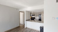 This single-floor unit is designed with a practical, open layout that connects the living and kitchen areas seamlessly. The kitchen is equipped with black stainless appliances, including a refrigerator, range, and microwave, complemented by gray-toned cabinetry, a subway tile backsplash, and a peninsula with a built-in sink and countertop overhang. A pantry with double doors provides additional storage within the kitchen. Wood-style luxury vinyl flooring runs throughout the main living areas, adding warmth and continuity to the space.

The living area benefits from a large window and sliding glass door access to an outdoor balcony, allowing substantial natural light to filter in throughout the day. A ceiling fan is centrally positioned in the main living space for added comfort. The bedrooms are well-proportioned, each featuring windows with horizontal blinds that allow for natural light and privacy control.

The bathroom is finished with a single-sink vanity topped with a light countertop, a large mirror, and a tiled shower-tub combination. Textured ceilings are consistent throughout the unit, and neutral gray walls provide a clean, versatile backdrop across all rooms.