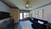 This single-floor residence offers a thoughtfully designed 1-bedroom, 1-bathroom layout that makes efficient use of its generous square footage. The living area serves as the heart of the home, featuring rich dark hardwood-style flooring that grounds the space with warmth and character. Crown molding adds a refined architectural touch, while a ceiling fan provides both style and practical comfort year-round. A textured ceiling adds subtle visual depth overhead. Natural light filters in through a set of windows and a glazed door that opens to the exterior, keeping the living space bright and connected to the outdoors. The living room offers ample room for seating and relaxation, with a neutral color palette on the walls that complements a variety of décor styles. A dark wood storage cabinet anchors one side of the room, providing additional functionality. The overall ambiance is warm, inviting, and well-balanced, combining practical features with tasteful design details. The single-floor plan ensures easy accessibility and a seamless flow throughout the home, making it an ideal space for comfortable everyday living.