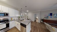 This single-floor residence offers a thoughtfully designed open-concept layout that seamlessly connects the kitchen, dining, and living areas. The kitchen is a standout feature, equipped with white shaker cabinetry, stainless steel appliances including a gas range and built-in microwave, a dishwasher, and a peninsula with a grey quartz countertop and undermount sink. Stylish pendant lighting hangs above the peninsula, adding a modern touch, while crown molding throughout the main living area lends an elegant finish.

The living space is bright and inviting, with wood-look plank flooring that runs consistently through the entire unit, and a large sliding glass door that brings in natural light. Two well-sized bedrooms provide comfortable retreats; the primary bedroom features a ceiling fan, a walk-in closet, and generous natural light from a large window. The secondary bedroom is equally comfortable with soft, neutral tones.

Both bathrooms are finished with white cabinetry, grey countertops, undermount sinks, and wood-look flooring, maintaining a cohesive aesthetic. Each bathroom includes a shower/tub combination with a clean, classic curtain setup. The overall ambiance of the residence is modern, clean, and functional, with a neutral color palette that creates a calm and welcoming atmosphere throughout.