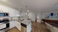 This single-floor residence offers a thoughtfully designed open-concept layout that seamlessly connects the kitchen, dining, and living areas. The kitchen is a standout feature, equipped with white shaker cabinetry, stainless steel appliances including a gas range and built-in microwave, a dishwasher, and a peninsula with a grey quartz countertop and undermount sink. Stylish pendant lighting hangs above the peninsula, adding a modern touch, while crown molding throughout the main living area lends an elegant finish.

The living space is bright and inviting, with wood-look plank flooring that runs consistently through the entire unit, and a large sliding glass door that brings in natural light. Two well-sized bedrooms provide comfortable retreats; the primary bedroom features a ceiling fan, a walk-in closet, and generous natural light from a large window. The secondary bedroom is equally comfortable with soft, neutral tones.

Both bathrooms are finished with white cabinetry, grey countertops, undermount sinks, and wood-look flooring, maintaining a cohesive aesthetic. Each bathroom includes a shower/tub combination with a clean, classic curtain setup. The overall ambiance of the residence is modern, clean, and functional, with a neutral color palette that creates a calm and welcoming atmosphere throughout.